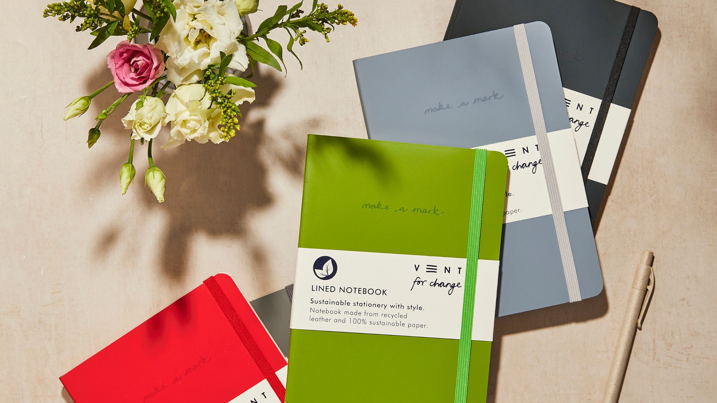 Eco-friendly stationery featuring notepads, notebooks, refillable pens and flowers on a green background